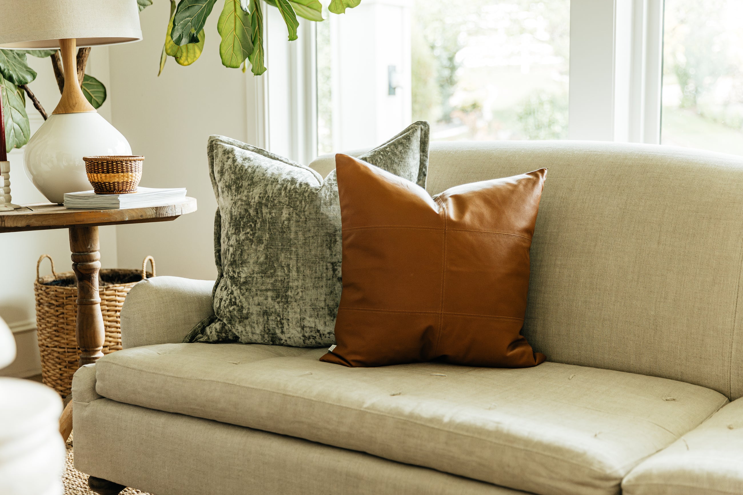 A light gray coach in a living room with an arrangement of velvet sage green and leather pillows.