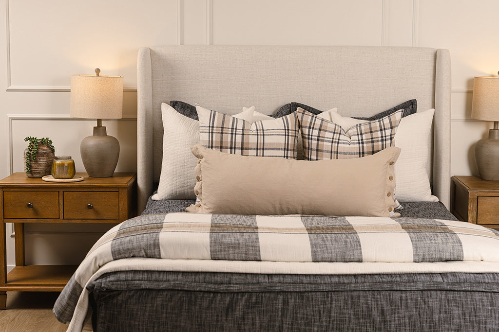 A bed made with dark charcoal gray zipper bedding and an assortment of neutral and plaid throw pillows and blanket.