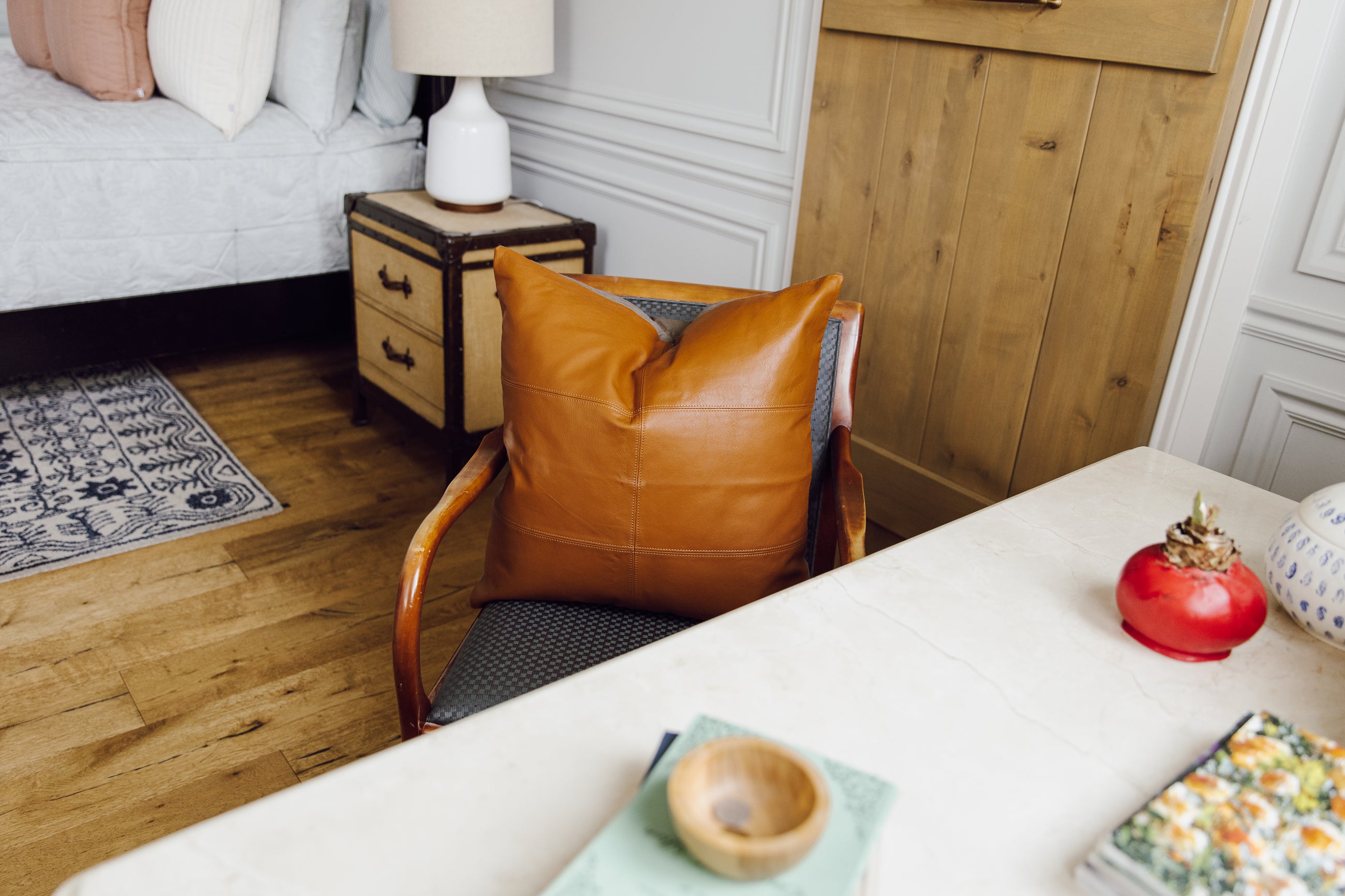 A neutral leather euro pillow with stitching arranged on a chair by a desk.