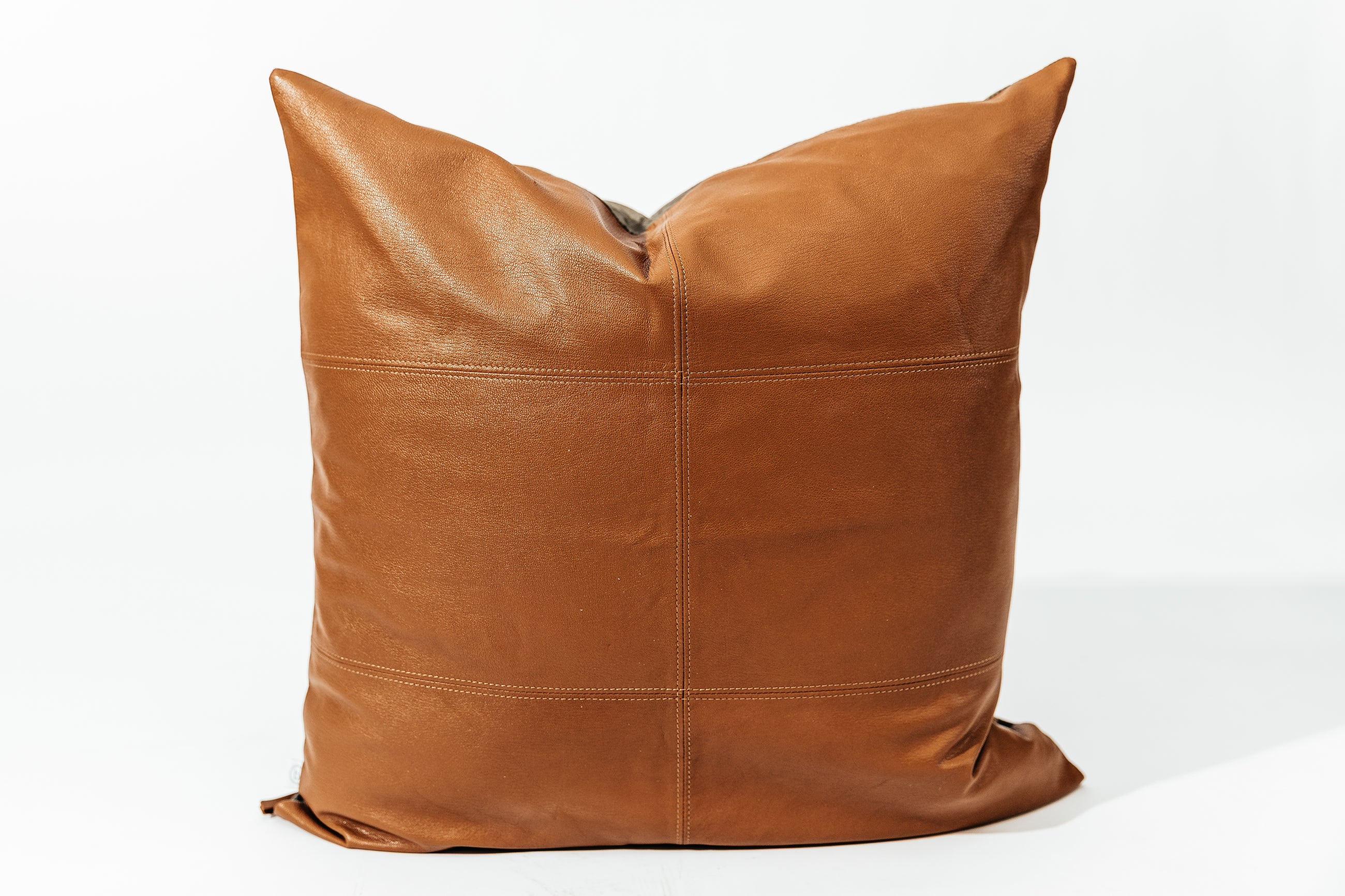 A neutral leather pillow with stitching arranged on a white background.