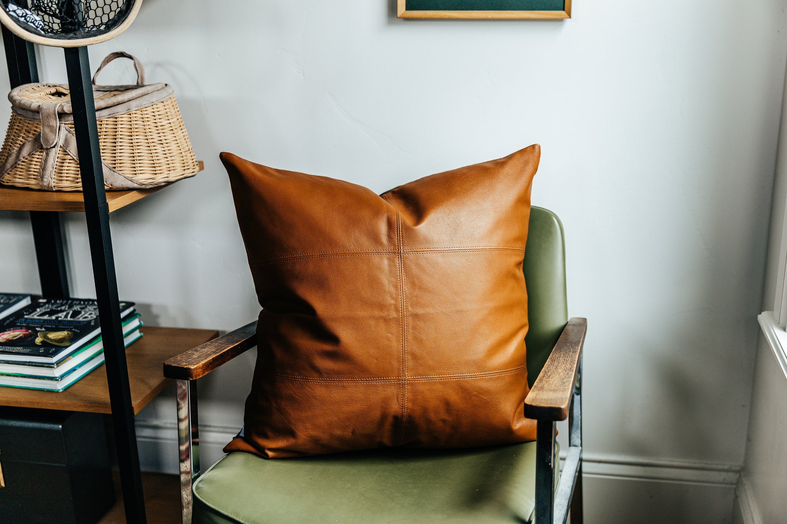 A neutral leather euro pillow with stitching arranged on a green chair.