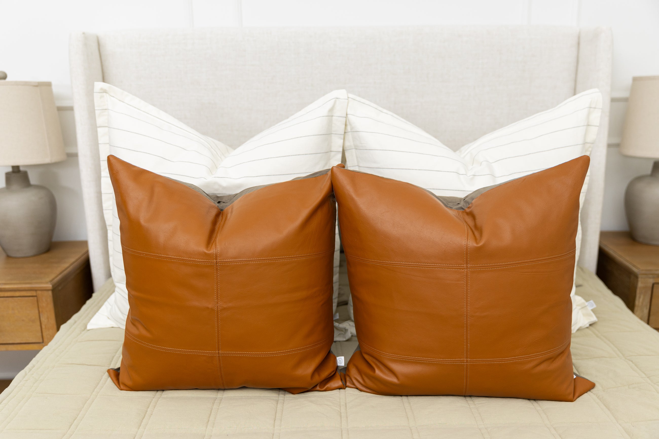 A bed made with khaki green zipper bedding adorned with neutral leather and white striped pillows.