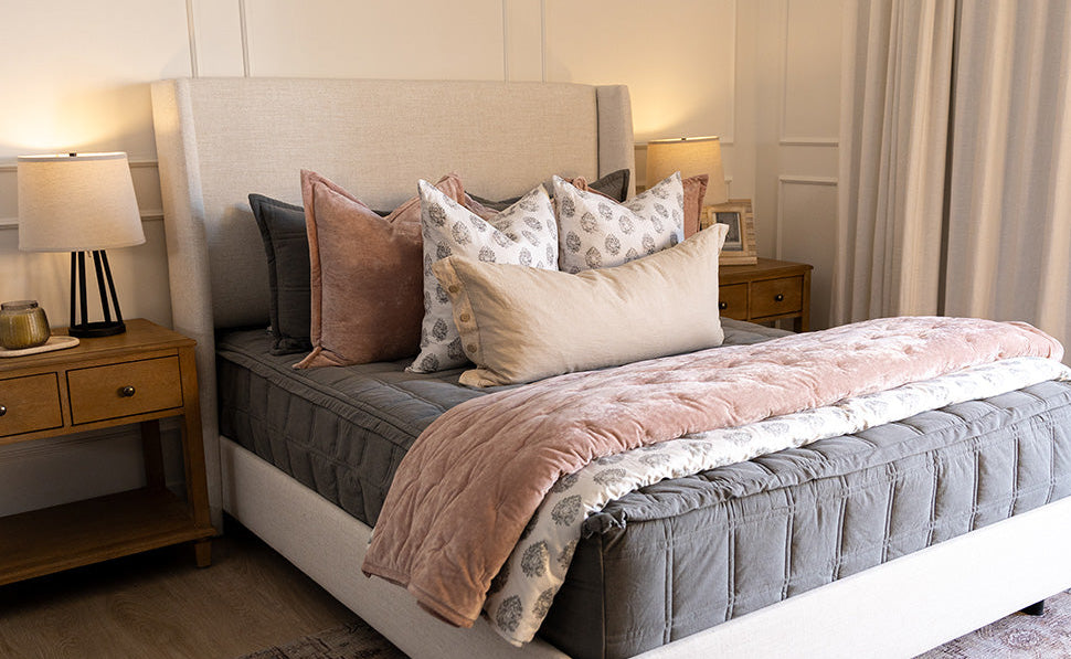 A bed made with gray zipper bedding and decorated with an assortment of floral and pink bedding accessories