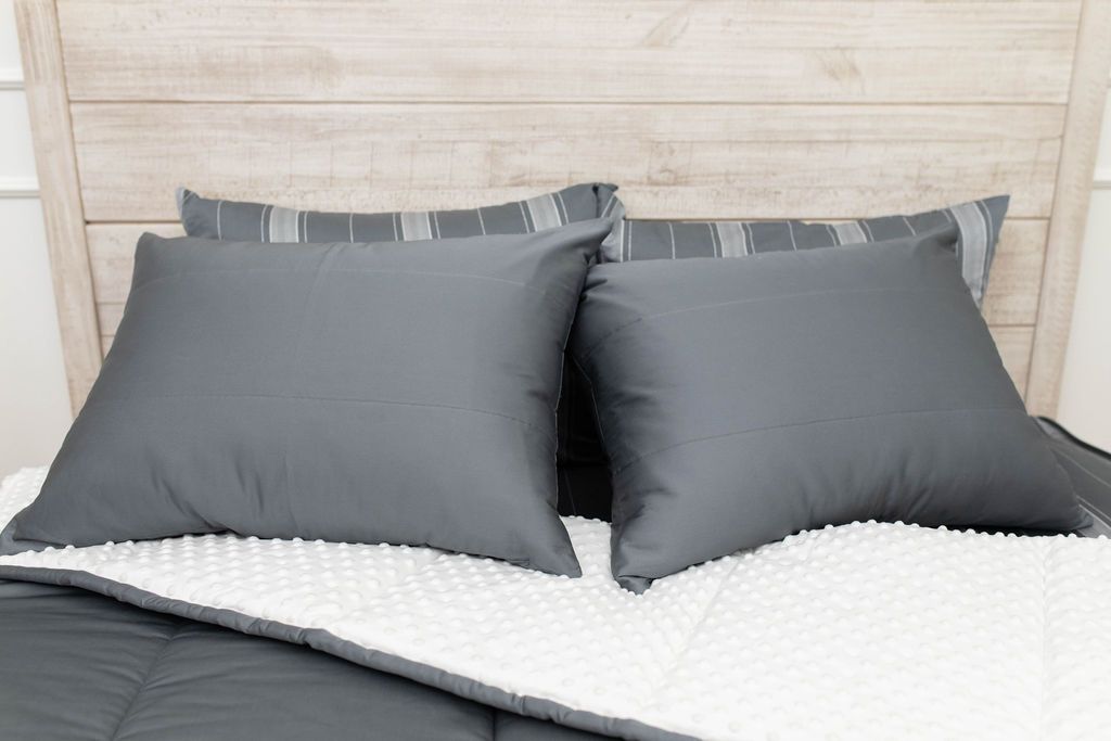 A gray zipper bedding with the white interior minky comforter pulled back and pillows on top of the bed.