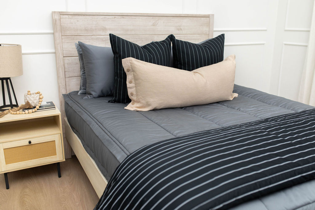 A queen bed made with gray zipper bedding and black striped and neutral pillows and blanket.