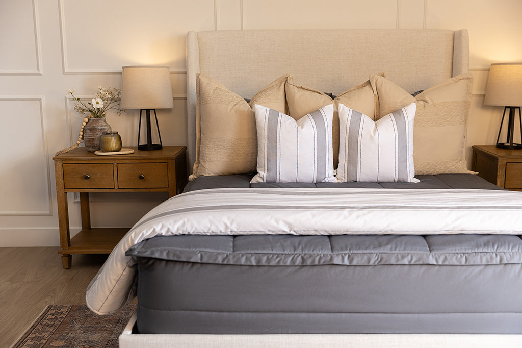 A bed made with gray zipper bedding and an assortment of neutral and striped throw pillows and blanket.