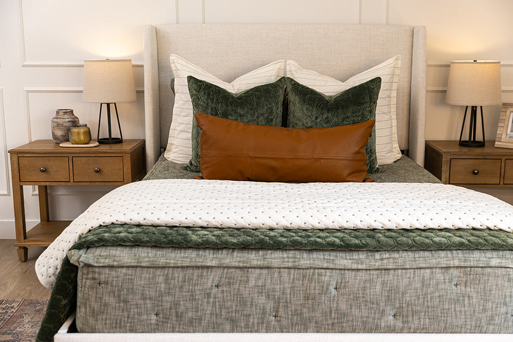 A bed made with deep emerald green zipper bedding and an assortment of neutral throw pillows and blankets.