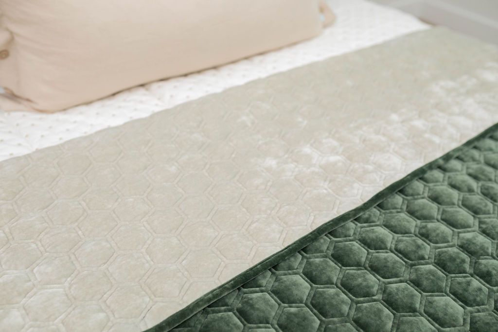 A close up of a bed made with cream embroidered zipper bedding and an emerald blanket laid on top of the bed with half of it fulled over to reveal the other side of the blanket which is a gray color.