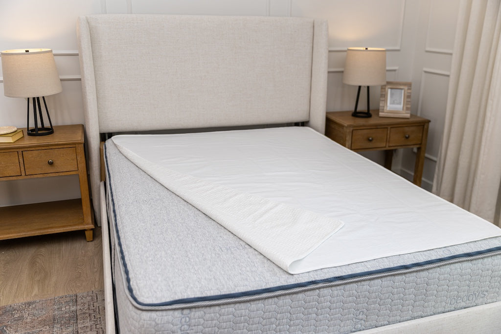 White absorbent accident bedding pad with a folded corner on a queen bed.