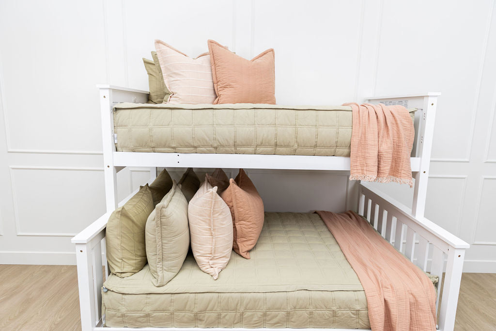 A bunk bed where both bunks are made with green zipper bedding and an assortment of light pink and terracotta bedding accessories.