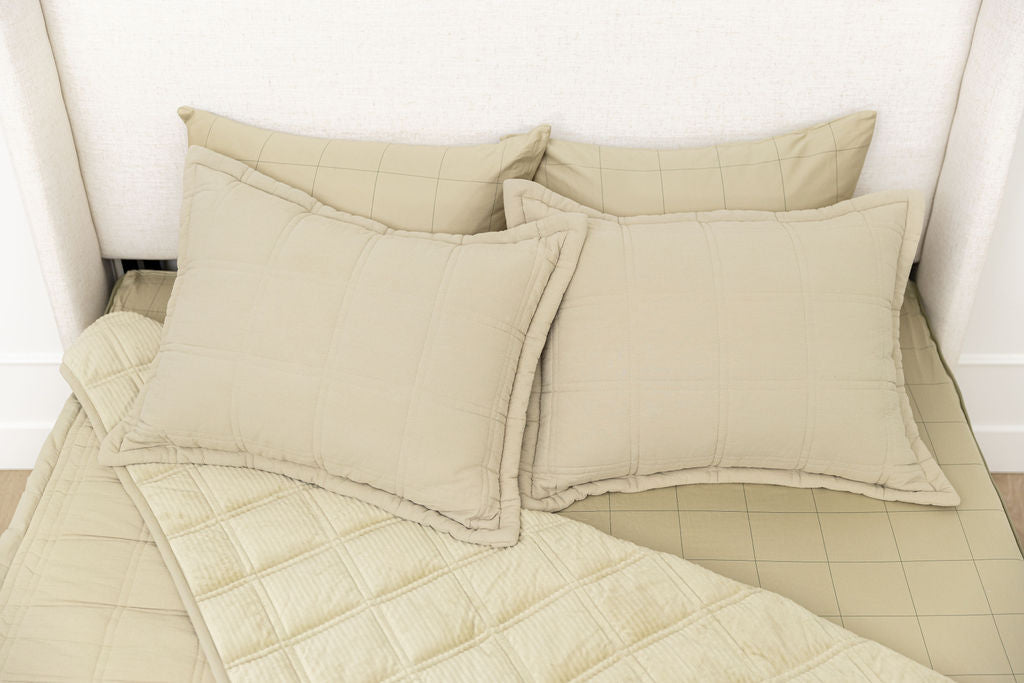A bed made with khaki quilted zipper bedding with the comforter pulled back showing minky interior lining and pillows on top of the bed.