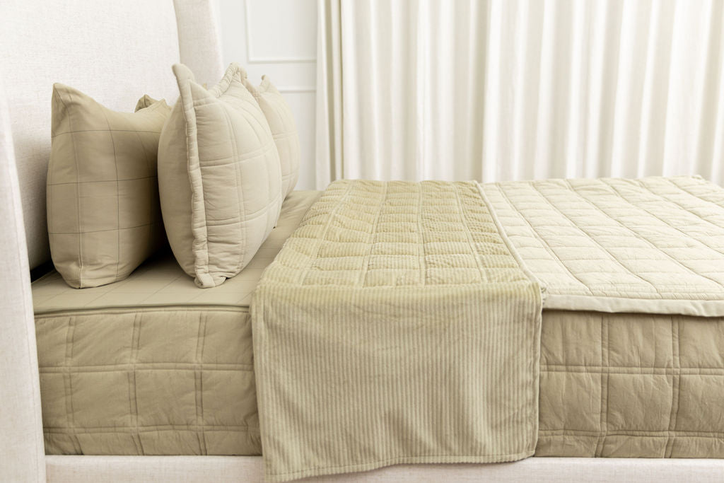 A bed made with green zipper bedding with the top portion unzipped and pulled back to reveal the inside lining.