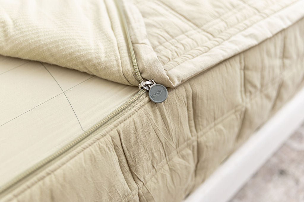 A close up on the zipper feature of a set of khaki green zipper bedding.