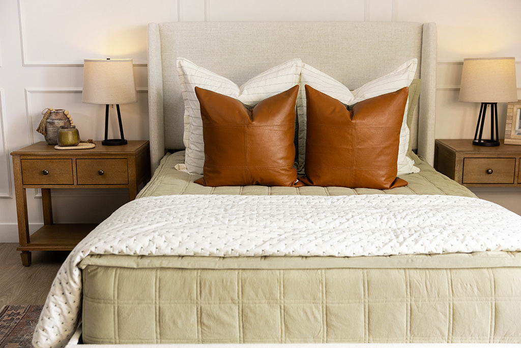 A bed made with khaki zipper bedding and an assortment of cream and leather bedding accessories.