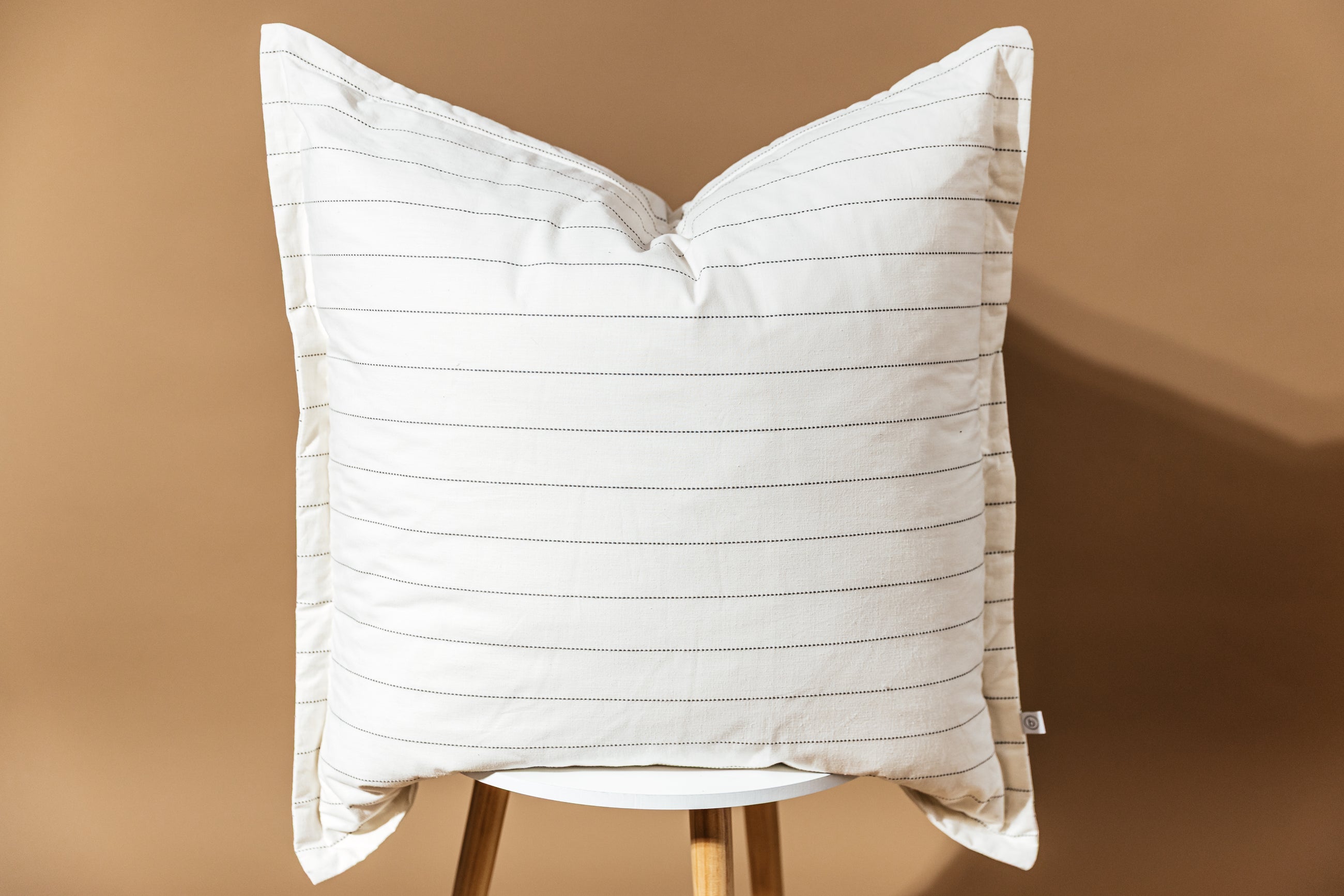 A cream XL euro pillow with green stripes arranged on a stool on a brown background.