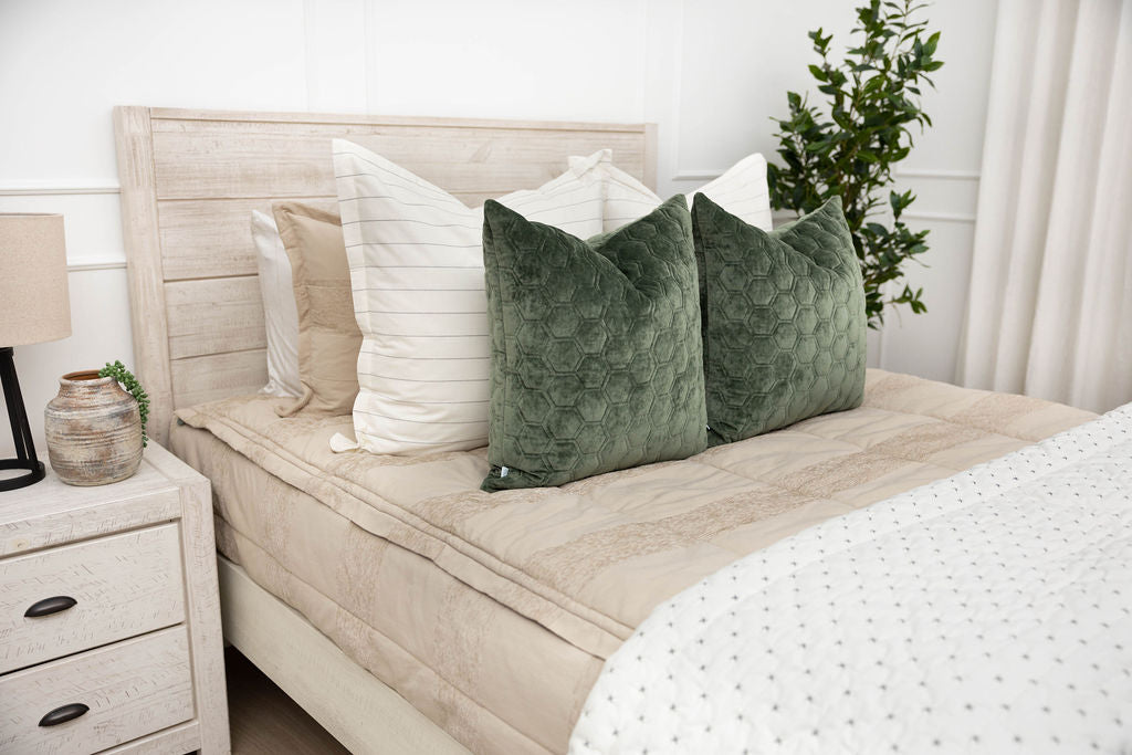 A brightly lit bedroom with a bed made with tan zipper bedding and neutral and velvet green pillows and blanket.