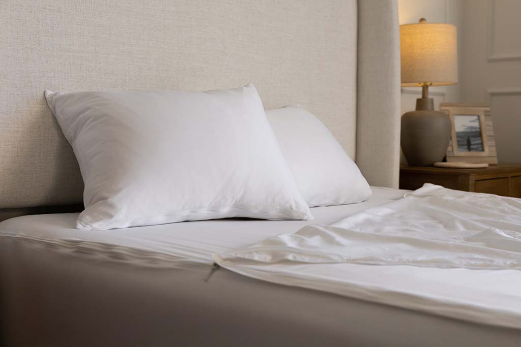 A side view of a bed made with white zipper sheets with the top sheet pulled back and pillows on top of the bed.