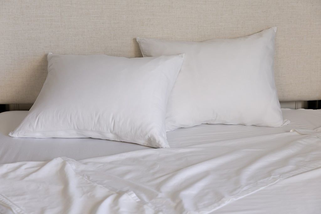 A bed made with white zipper sheets with the top sheet pulled back and pillows on top of the bed.