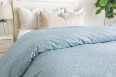 Light blue duvet on white zipper bedding styled with white, teal, and cream pillows