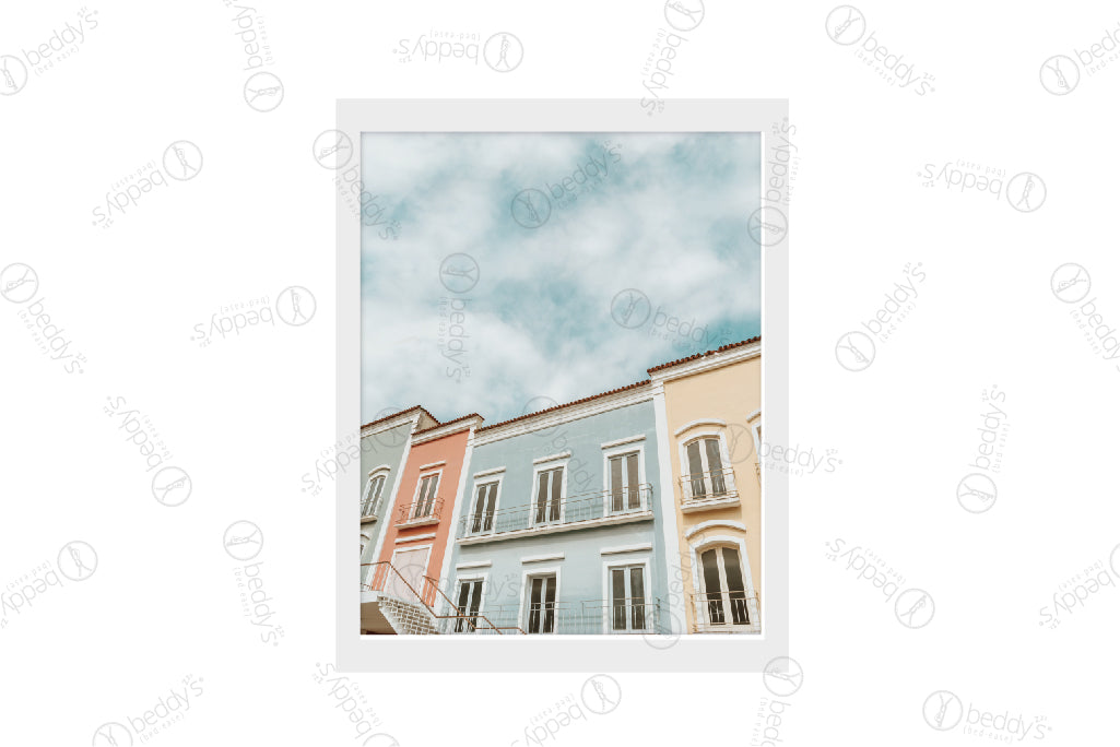 Blue, light red, and yellow attached buildings with a blue cloudy sky digital artwork showcased in a frame.