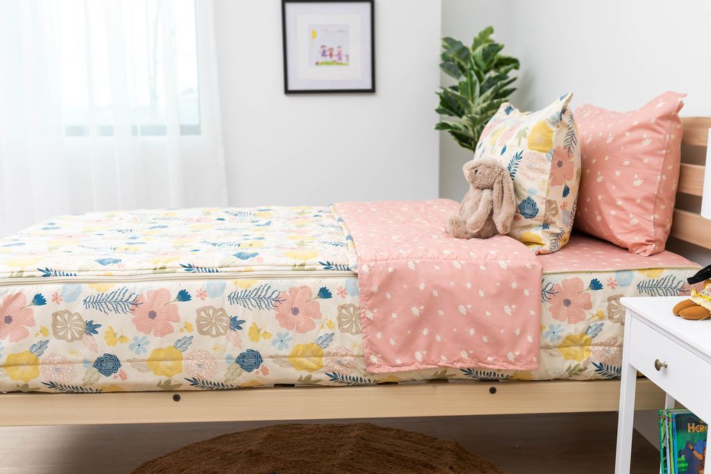 A side shot of a twin bed made with pink, yellow, and blue floral kids zipper bedding, the top unzipped and pulled back slightly and two pillows at the head of the bed.