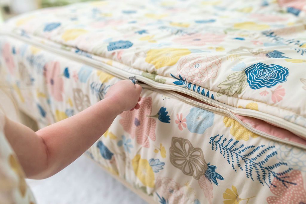 A young girl pulling the zipper closed on a set of yellow, pink, and blue floral kids zipper bedding.