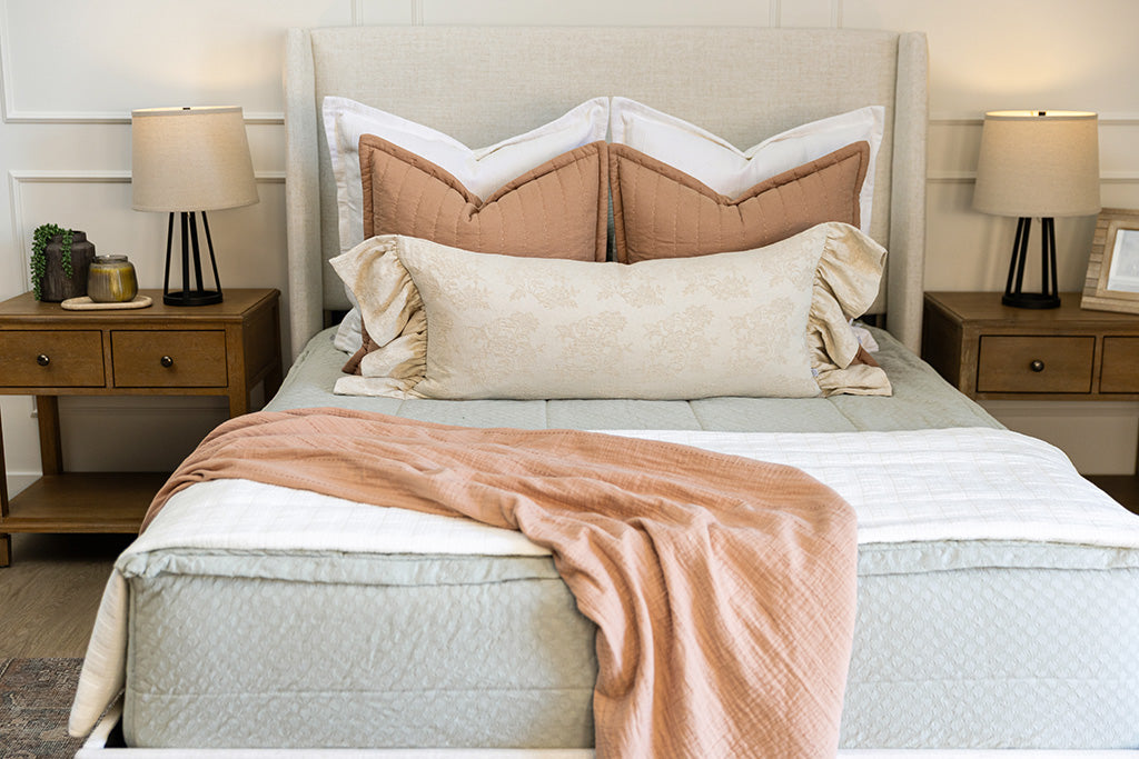 A bed made with soft green zipper bedding and an assortment of pink, cream, and white pillows and blanket.