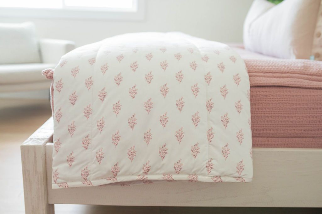 A side view of a bed made with pink woven zipper bedding with a pink floral pattern white blanket folded over the end of the bed.