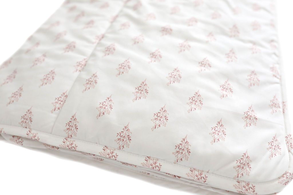 A folded floral pink pattern white blanket on a white background.