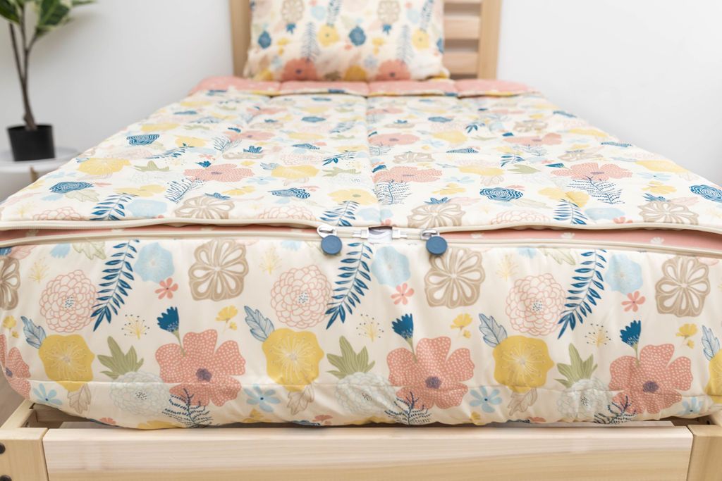 The foot of a bed made with yellow, pink, and blue floral kids zipper bedding showing where the two zippers are located.