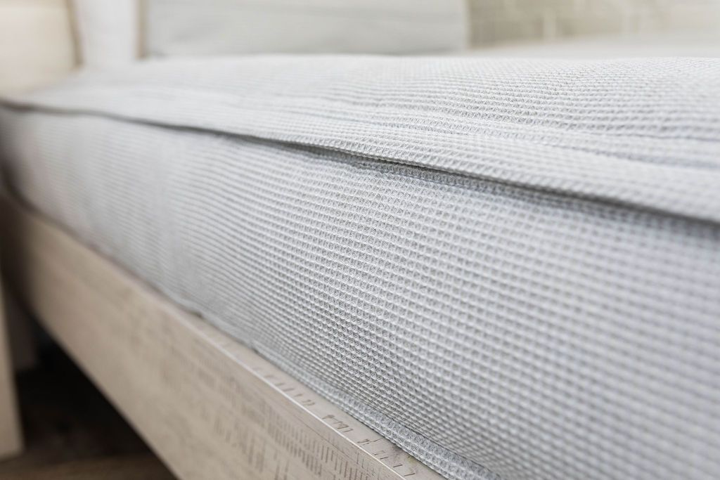 A close up side view of a bed made with light gray waffle textured zipper bedding.