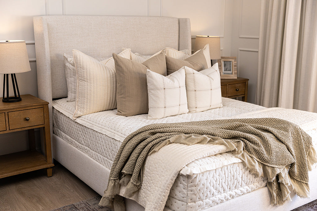 A bed made with cream embroidered zipper bedding, decorated with neutral throw pillows and blanket.