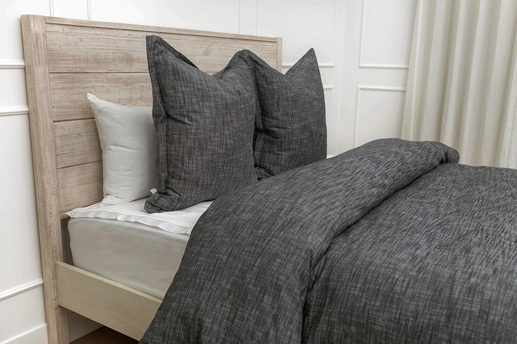 A side view of a bed made with a gray zipper sheet set and a textured white zipper duvet and matching white and gray pillows.