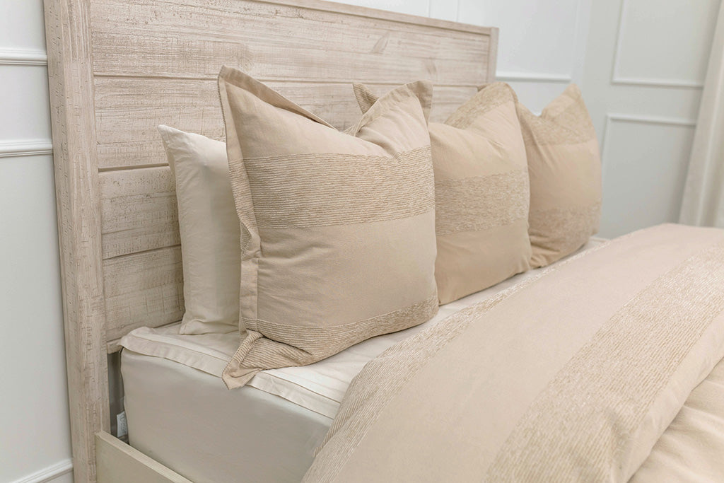 A side view of a bed made with a white zipper sheet set and a white and tan textured zipper duvet and matching pillows.