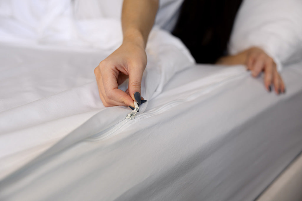 A close up view of a person zipping up a white zipper sheet set.