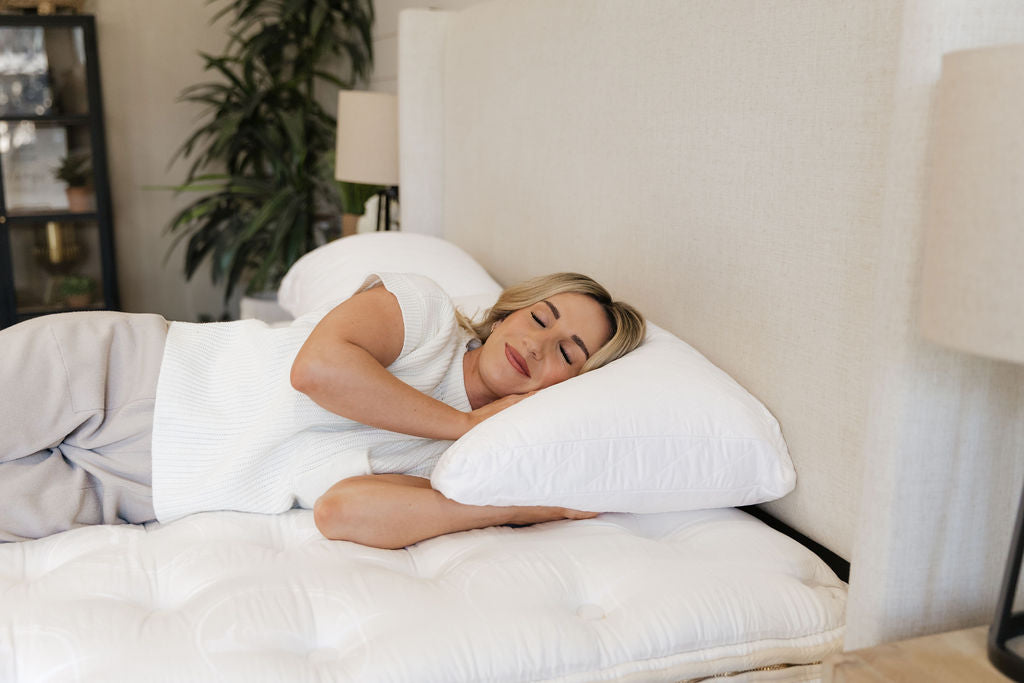 
      woman peacefully resting on a white pillow and mattress topper in a bedroom
    