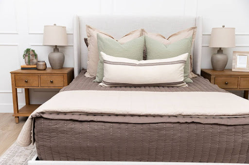 
      A bright room featuring a bed with a gray headboard and brown zipper bedding, as well as a throw blanket and throw pillows.
    