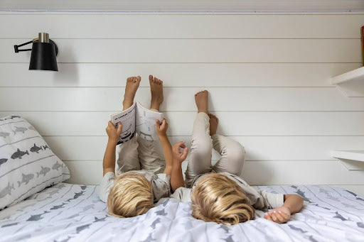 
      two boys laying on a bed with zipper bedding readying a book together.
    