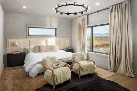 
      A primary bedroom with a bed made with a white duvet and neutral bedding accessories, as well as fluffy, fur lined chairs at the foot at the foot of the bed.
    