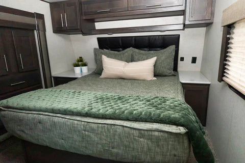 
      An RV bed made with green zipper bedding and a green velvet blanket at the foot of the bed.
    