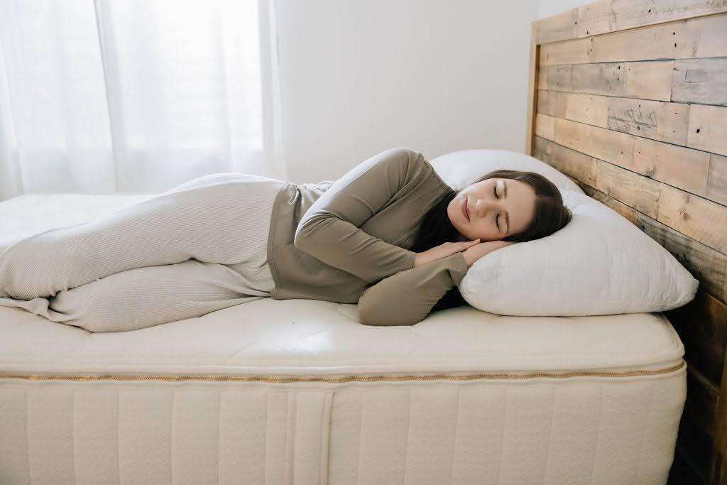 
      woman in green shirt sleeping peacefully on white organic mattress with rustic wooden headboard
    