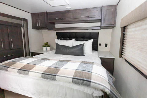 
      An RV bed made with white zipper bedding and a plaid blanket folded up at the foot of the bed.
    