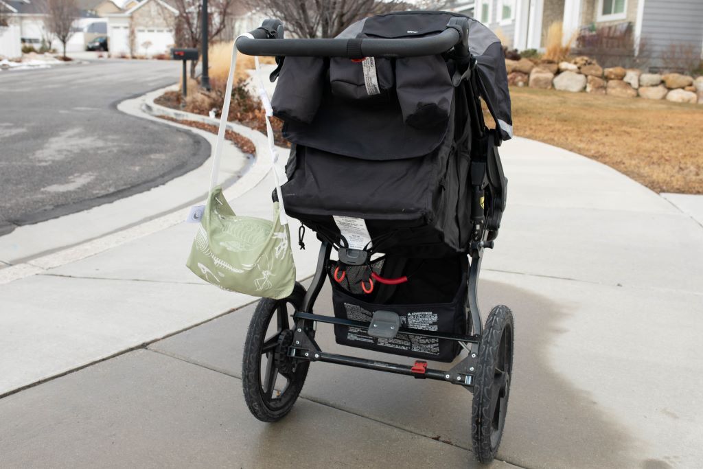 A bag holding a blanket inside hanging off the side of a stroller