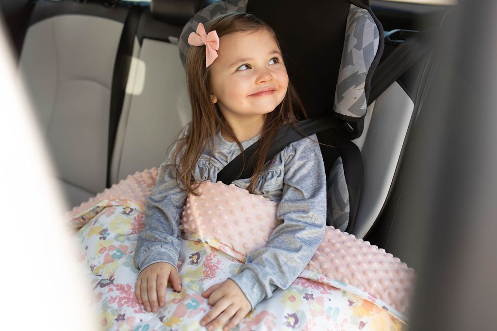 Child in car booster seat with floral mini blanket