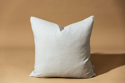 A light gray pillow on a brown backdrop.