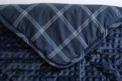 A navy blue plaid mini blanket folded over to reveal the minky interior.