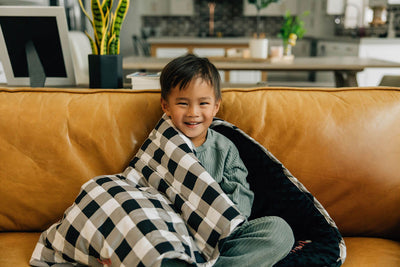 Little boy cuddling on couch in a white, black and gray child's blanket