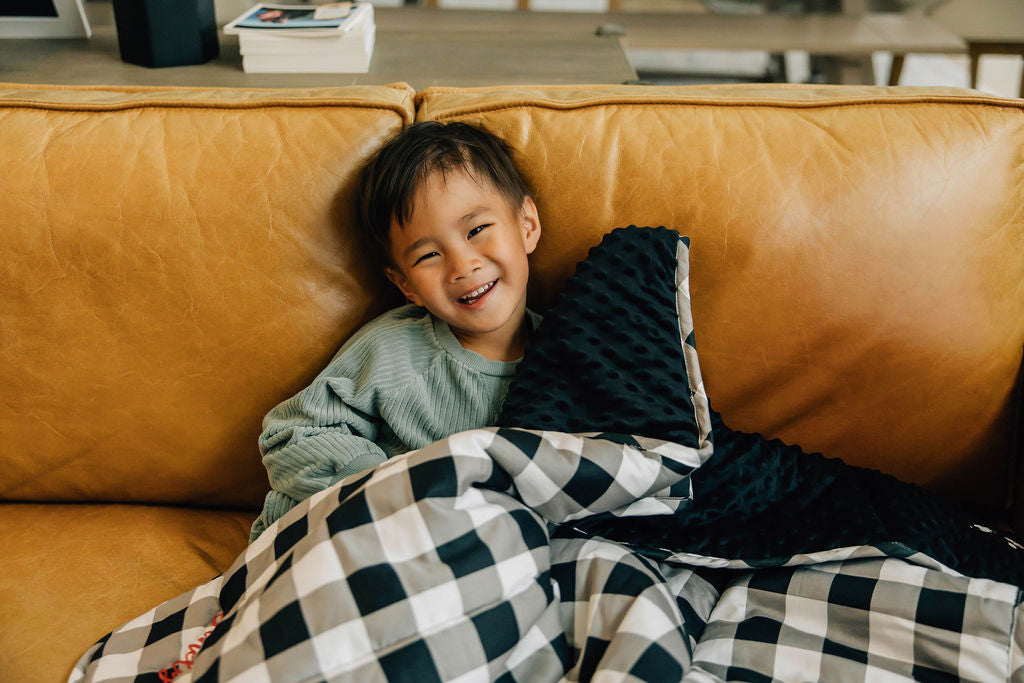 Little boy cuddling on couch with white, black and gray child's blanket
