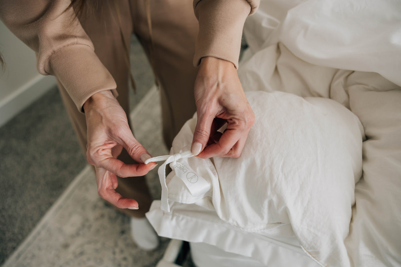 A woman tying her duvet insert in place using the interior ties and loops on her duvet insert and cover.