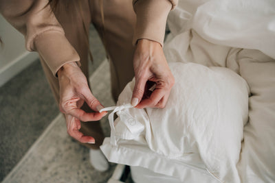 A woman tying her duvet insert in place using the interior ties and loops on her duvet insert and cover.